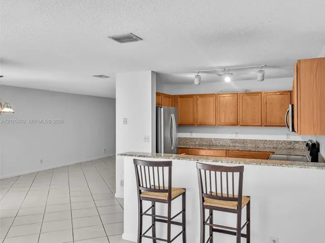 Kitchen featuring light wood cabinetry, stone-surface countertops, stainless steel appliances, and a tiled breakfast bar