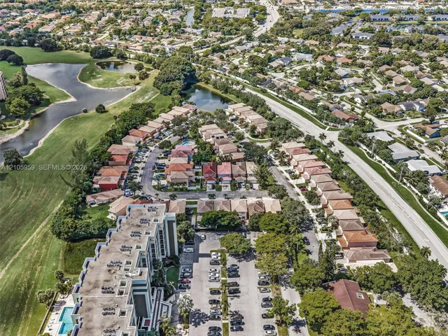 Aerial perspective featuring a multi-story residential building, an attached swimming pool, a dedicated parking lot, and proximity to expansive green spaces and water features