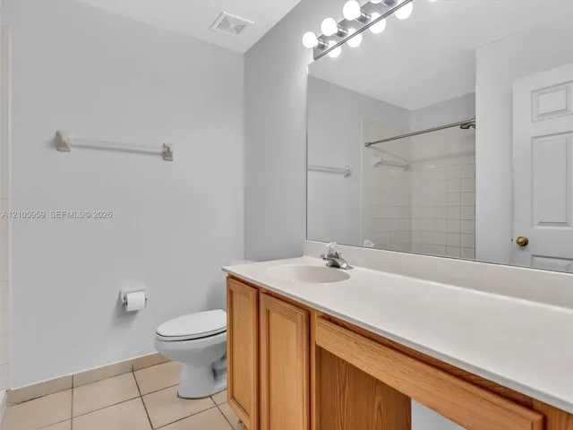 Bathroom featuring wood-finish cabinetry, an expansive integrated countertop with a single-basin sink, a full-width vanity mirror, a polished chrome multi-bulb light fixture, and tile flooring