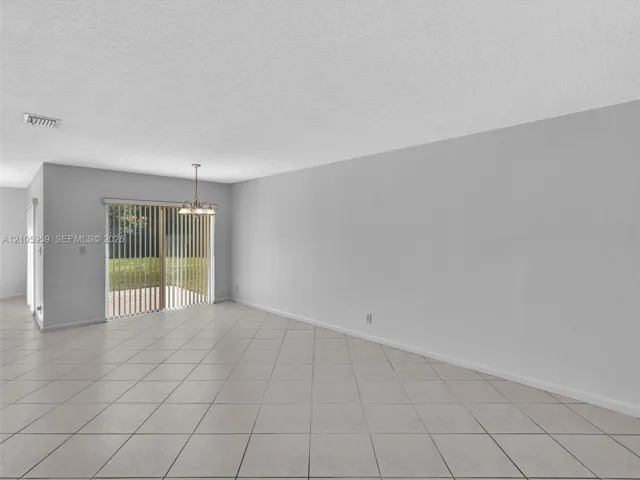 Interior space featuring neutral tile flooring, light-toned walls, a textured ceiling, and a multi-light chandelier fixture with a glass-paned sliding door