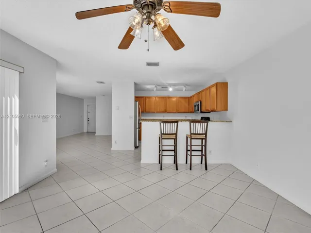 Ceramic tile flooring throughout, kitchen featuring wood cabinetry, stone-finish countertops, stainless steel appliances, and a ceiling fan with integrated lighting