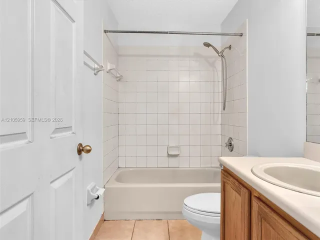 Bathroom featuring square-tile shower surround, handheld shower fixture, wood-finish cabinetry, integrated basin, and tiled flooring