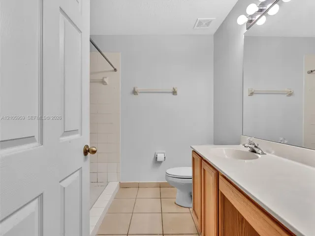 Bathroom featuring wood-finish cabinetry, a white countertop with an integrated basin, tile flooring, and a shower area with tiled surround