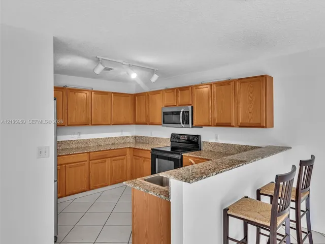 Kitchen featuring wood cabinetry, stone-surface countertops, tile flooring, integrated microwave, and adjustable track lighting
