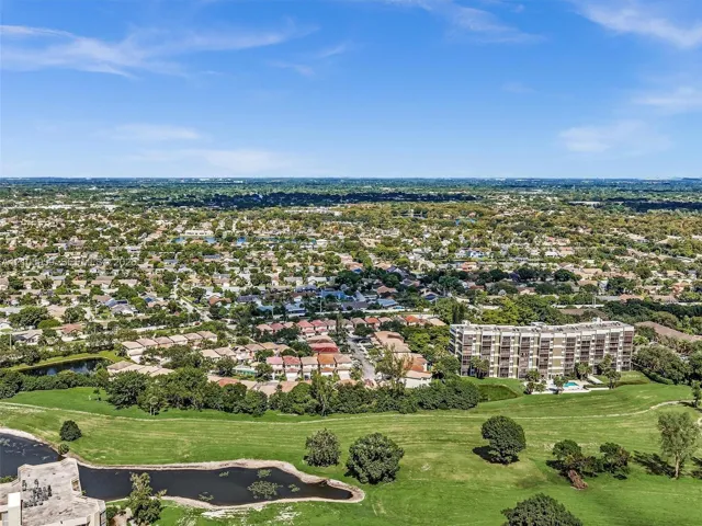 Aerial perspective of the residential area featuring a multi-story building, an expansive grass-covered expanse, and a natural pond