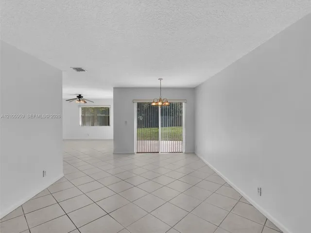 Neutral tile flooring, sliding glass patio door, multi-arm chandelier, and textured ceiling finish