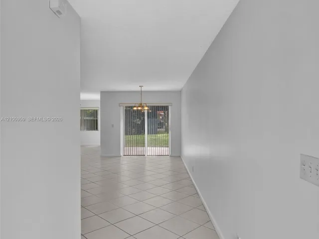 Neutral-toned tile flooring, multi-light hanging chandelier, and sliding glass doors with vertical blinds