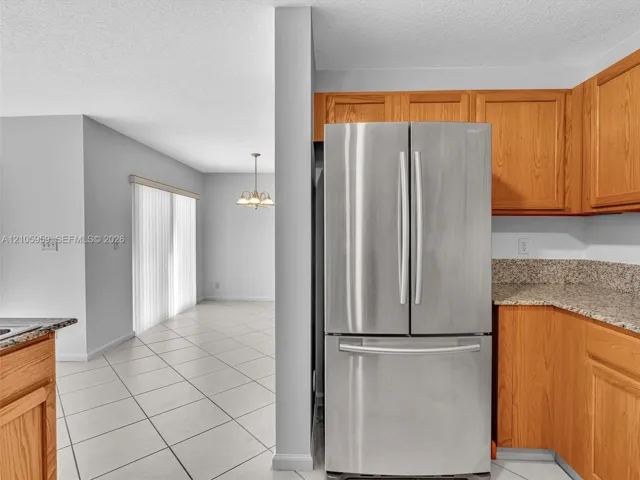 Kitchen featuring light-finish wood cabinetry, speckled stone-composite countertops, and a stainless steel French-door refrigerator with a bottom-mount freezer