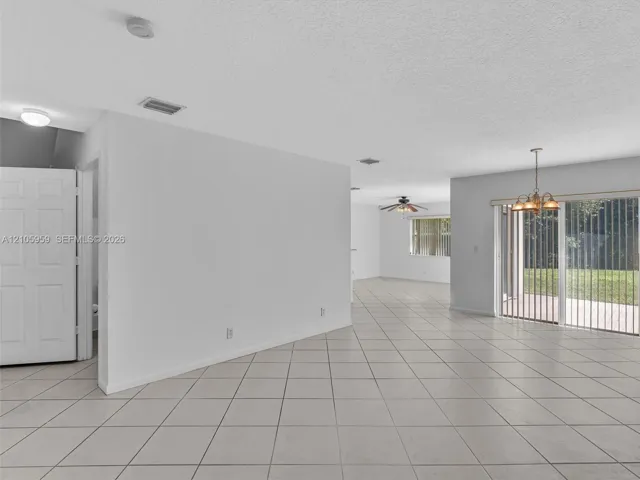 Open-concept interior featuring large-format neutral tile flooring, multi-pane sliding glass doors, a decorative multi-light chandelier, and recessed ceiling lighting