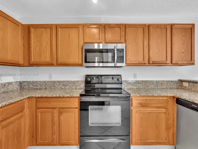 Kitchen featuring natural-finish wood cabinetry, stone-patterned countertops, and black-finish built-in appliances including a microwave and oven range