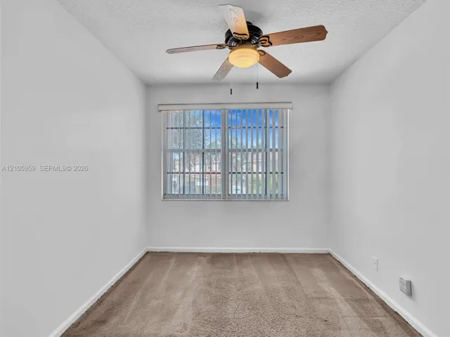Neutral-toned wall interior featuring carpeting, a ceiling fan with integrated lighting, and a multi-pane window with vertical blinds