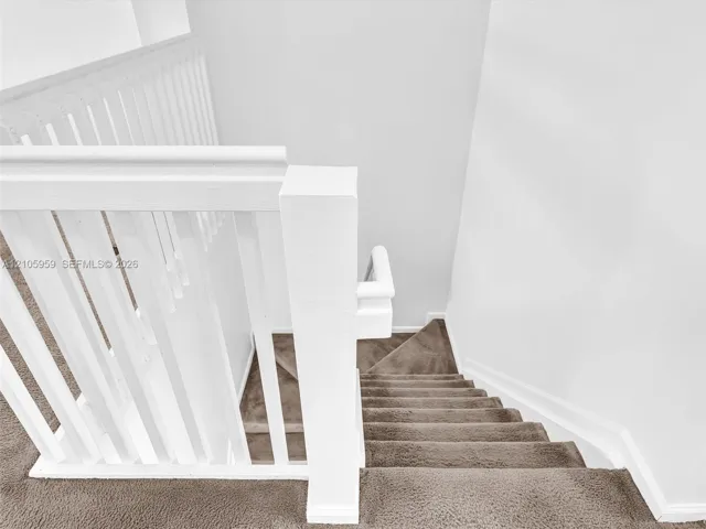 Staircase featuring a white balustrade with a square newel post and neutral carpeting