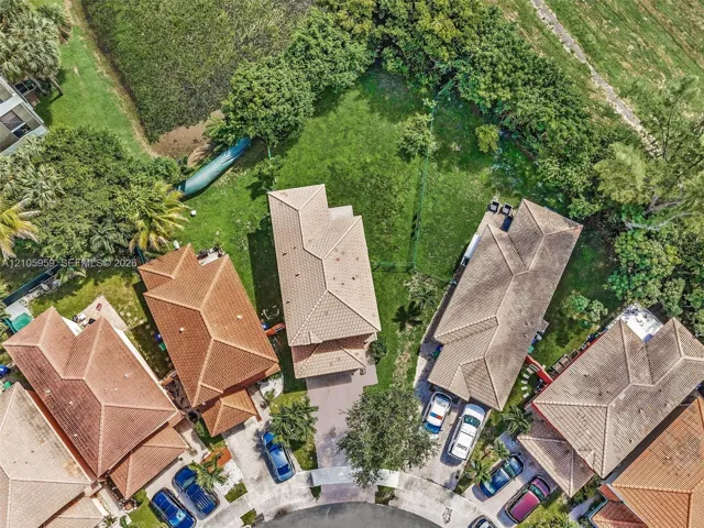 Aerial perspective of a multi-story residence featuring a tile roof, paved driveway, and expansive grass yard with mature perimeter landscaping
