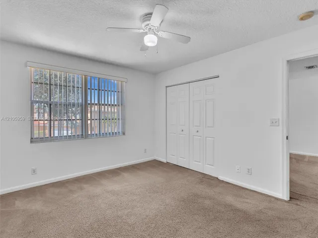 Neutral-toned carpeting, white walls, dual-panel closet doors, white ceiling fan with integrated lighting, and window with vertical blinds