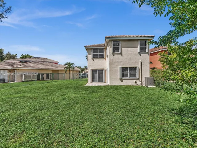 Two-story residence featuring a stucco exterior, concrete tile roofing, sliding glass door, and a fenced backyard with lawn space