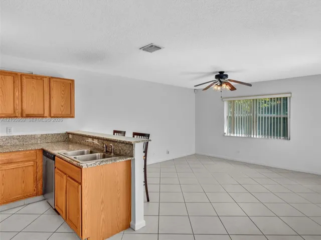 Kitchen featuring light wood cabinetry, stone-finish countertops, dual-basin stainless steel sink, tiled flooring, and a ceiling-mounted light fixture