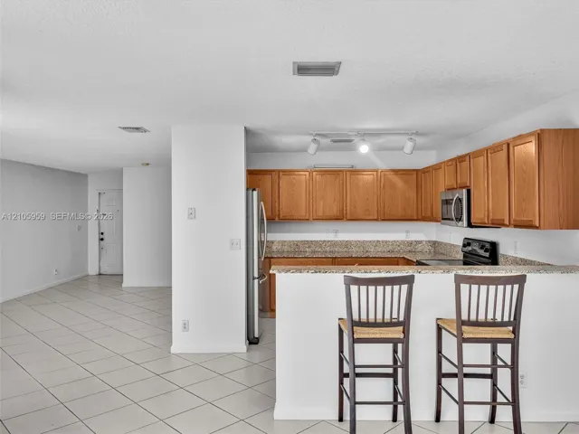 Kitchen featuring wood cabinetry, stone-surface countertops, tile flooring, stainless steel refrigerator, and integrated track lighting
