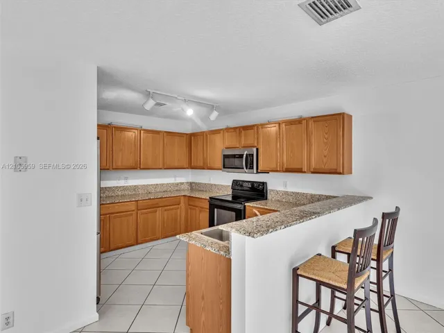 Kitchen featuring wood cabinetry, stone-surface countertops, tile flooring, built-in microwave, and track lighting