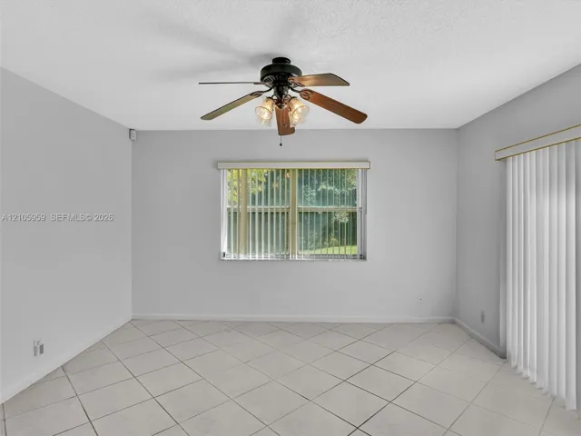 Neutral-toned tile flooring, ceiling fan with integrated light fixture, window with vertical blinds, and glass sliding door with vertical blinds