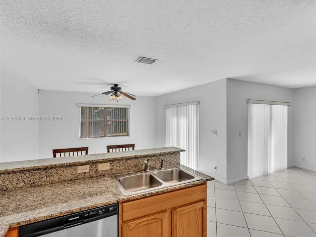 Kitchen featuring a stone-pattern countertop, dual-basin stainless steel sink, wood-finish cabinetry, stainless steel dishwasher, and tile flooring