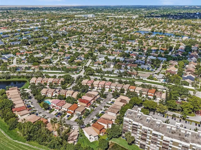 Aerial perspective of a suburban landscape featuring a dense collection of residential structures, mature tree canopy, multiple community ponds, and paved street networks