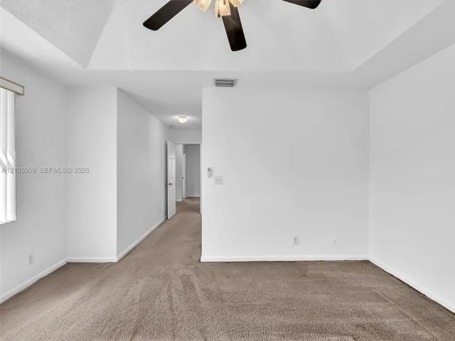 Tray ceiling featuring a dark-finish ceiling fan and neutral-toned wall-to-wall carpeting