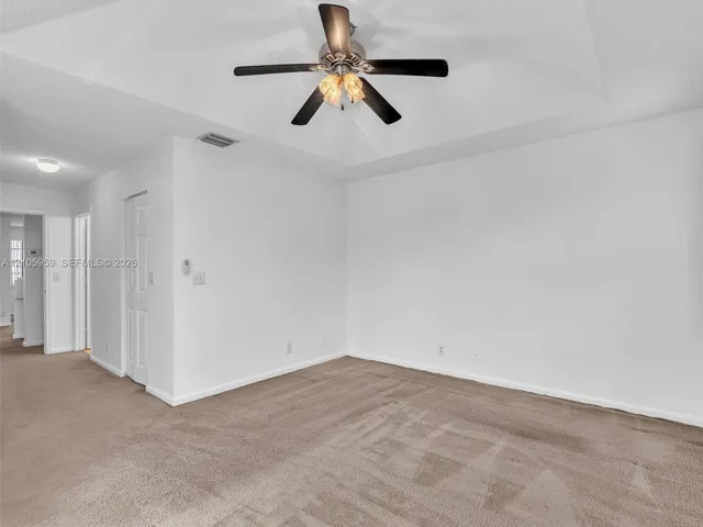 Tray ceiling featuring a central multi-blade ceiling fan with integrated light fixture, neutral wall-to-wall carpeting, and multi-panel interior door