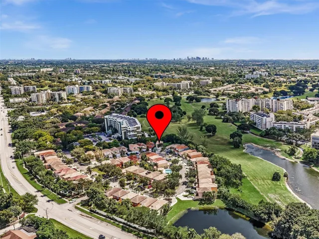 Aerial perspective of a multi-unit residential complex featuring tile roofing and integrated common area pool, situated among expansive green spaces and water features