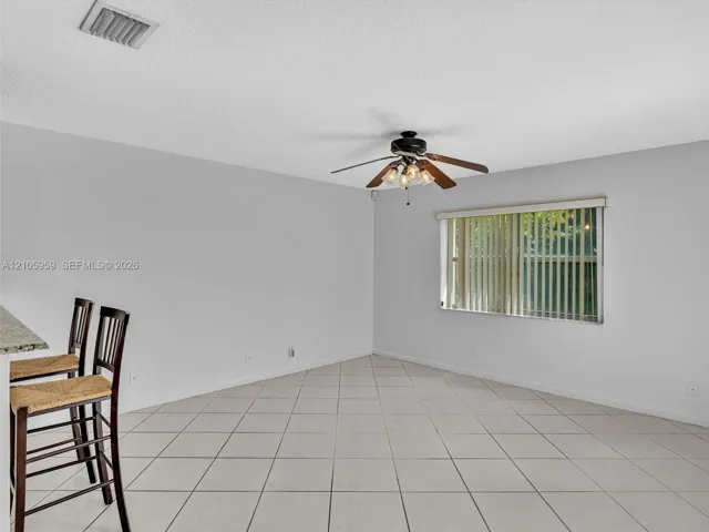 Neutral-toned ceramic tile flooring, ceiling fan with multi-light fixture, and large window with vertical blinds