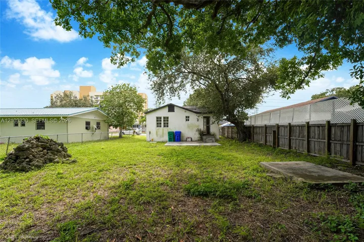 Expansive backyard featuring a large tree, perimeter wood fencing, and a concrete patio slab