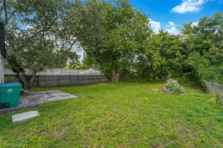 Backyard featuring a paved patio area, mature trees, wood privacy fencing, and a stone garden feature