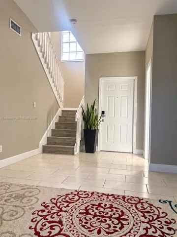 Tile flooring, staircase with wood-finish treads, window with grid pattern, white paneled door, and neutral wall paint