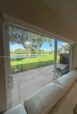 Sliding glass doors opening to a concrete patio, featuring a manicured lawn and a body of water in the background