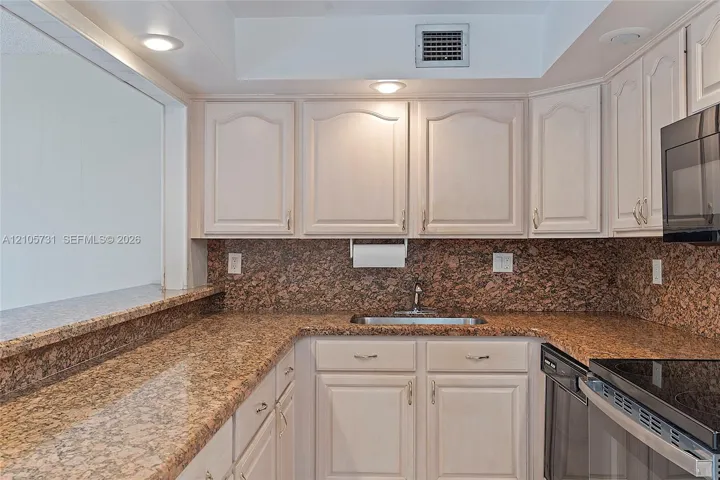 Kitchen featuring stone countertops, stone tile backsplash, light-finish cabinetry, built-in black microwave, and recessed lighting