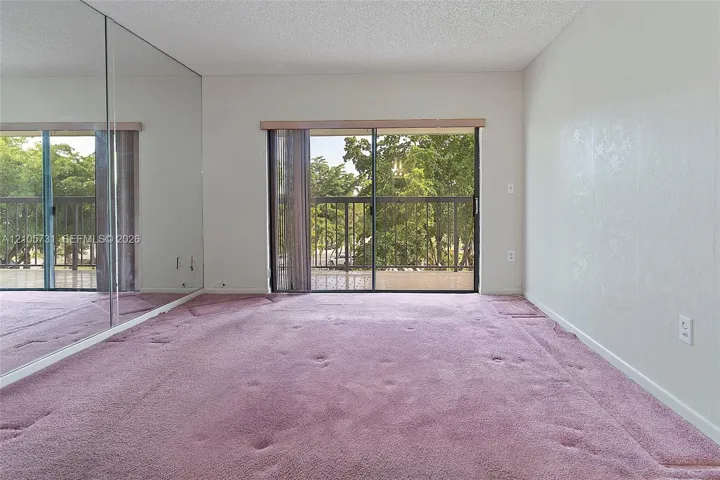 Room featuring a wall of floor-to-ceiling mirror panels, carpeted flooring, and a sliding glass door providing external access to a balcony with metal railings
