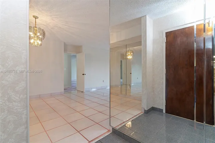 Entryway featuring a stone-tile floor, floor-to-ceiling mirrored wall panels, decorative multi-tiered pendant lighting, and a solid wood door with brushed metal trim