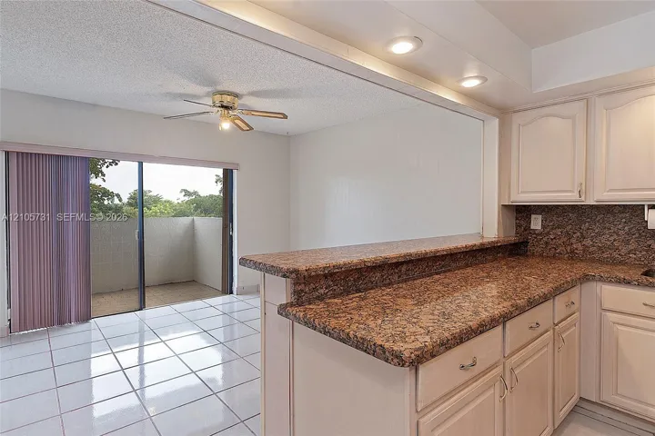 Kitchen featuring cabinetry with crown molding, stone-finish countertops, recessed lighting, white tile flooring, and a sliding glass door