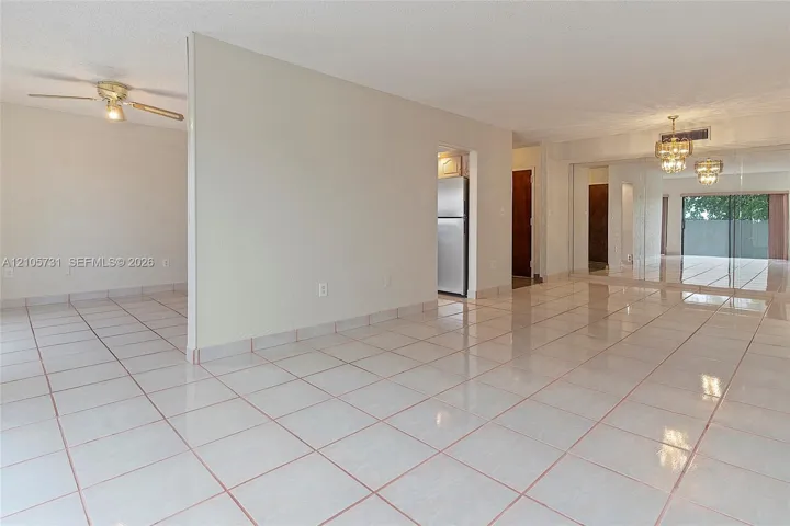 Open-concept interior featuring light-toned tile flooring, mirrored sliding closet doors, a dual-arm ceiling fan, and ornate overhead lighting fixtures