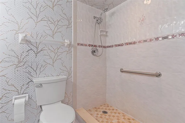 Bathroom featuring a tiled walk-in shower with chrome hand-held showerhead, integrated metallic accent tile border, chrome grab bar, and patterned wall covering