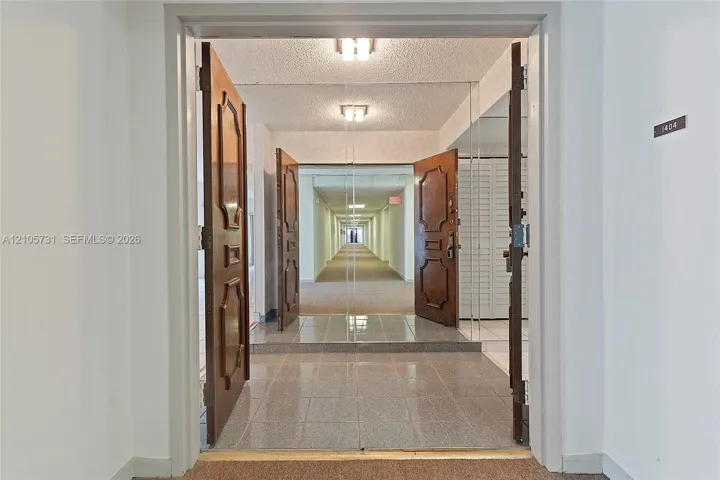 Entryway featuring double solid-wood doors with decorative panels, polished stone-finish floor tiling, and integrated wall-to-wall mirror paneling