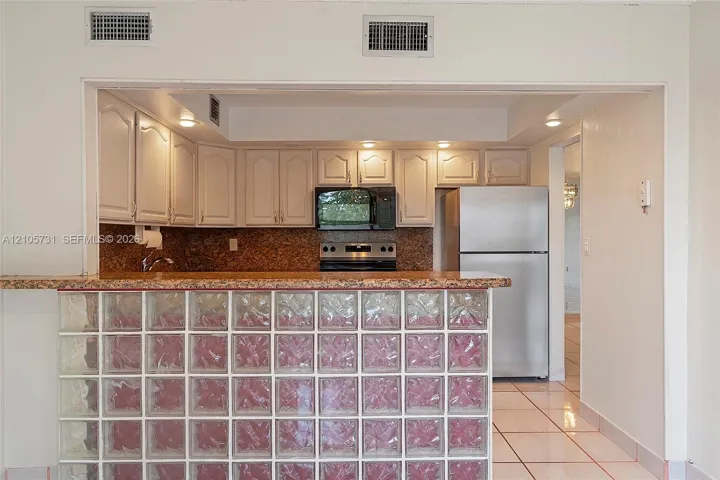 Kitchen featuring white cabinetry, stone-finish countertops, stainless steel appliances, and a glass block breakfast bar