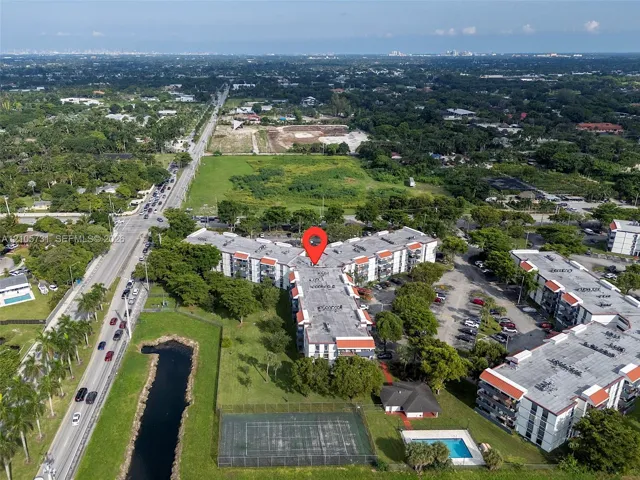 Aerial view featuring multi-story residential buildings, an outdoor swimming pool, and a fenced tennis court