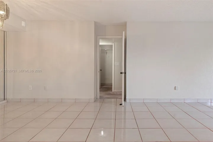 Neutral ceramic tile flooring and interior swing door leading to a walk-in closet with built-in shelving