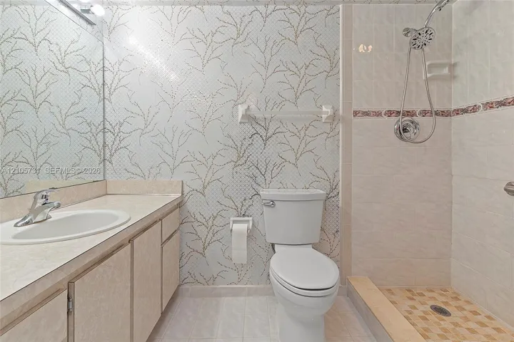Bathroom featuring a vanity with an integrated sink, patterned wall covering, floor-to-ceiling mirror, and a walk-in shower with a handheld fixture and decorative tile accent border