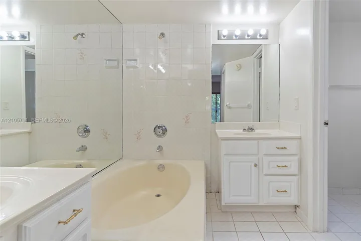 Bathroom featuring a vanity with integrated sink, porcelain tile flooring, full-width wall mirror, and a bathtub with tiled surround