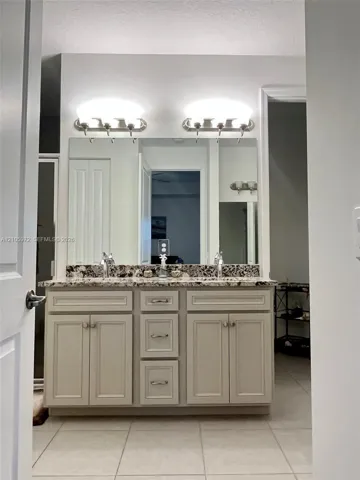 Double-sink vanity featuring neutral-toned cabinetry, a stone-patterned countertop, a large wall-mounted mirror, and dual light fixtures