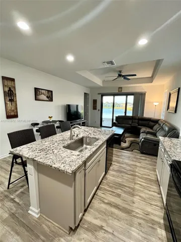 Kitchen island featuring a stone countertop, undermount stainless steel sink, wood-finish flooring, recessed lighting, and tray ceiling