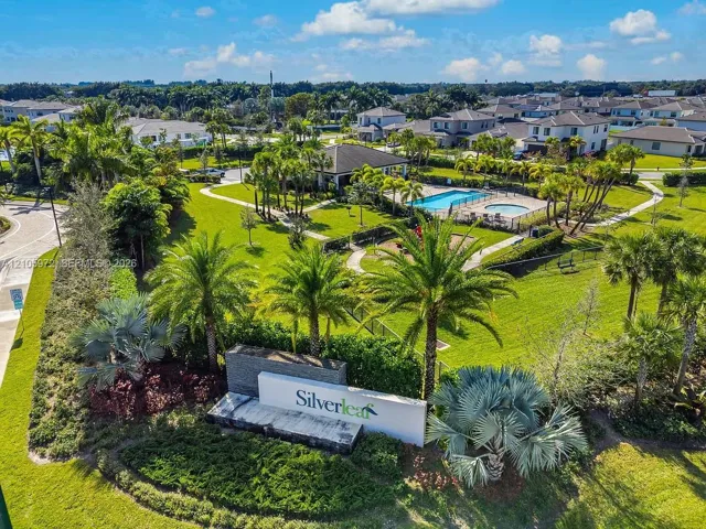 Aerial view of community grounds featuring a swimming pool, spa, playground, landscaped green spaces, and palm tree-lined walkways