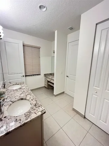 Bathroom featuring a dual-sink vanity with stone-surface countertops, recessed lighting, tile flooring, and a dedicated vanity seating area with integrated cabinetry