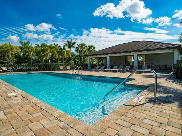In-ground swimming pool with a stone paver deck, stainless steel handrails, integrated steps, and a covered lanai